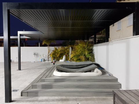 Black freestanding aluminum pergola over a raised spa deck, photographed at dusk