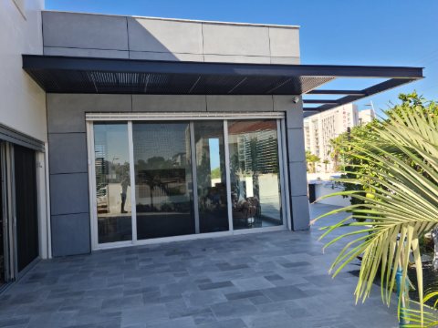 Dark grey aluminum pergola projecting from a modern facade over a stone patio and glass sliding doors