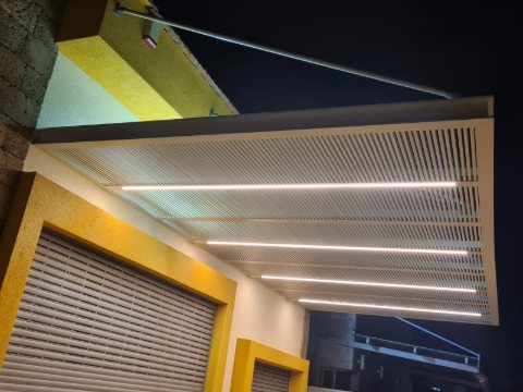 White aluminum pergola with LED strip lighting, supported by tension rods above a garage, at night